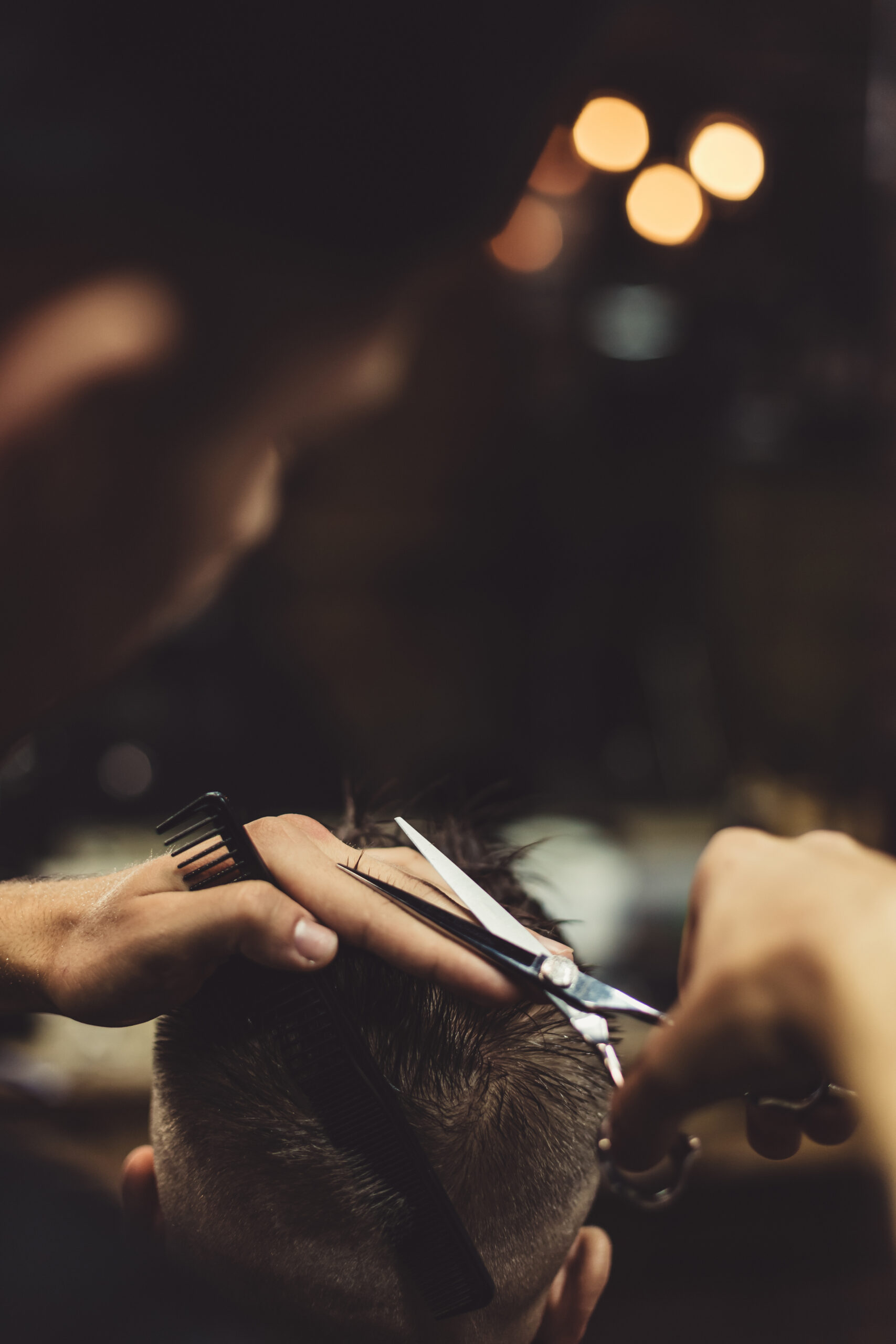 Anonymous stylish barber with tattoos cutting hair of male client in chair.