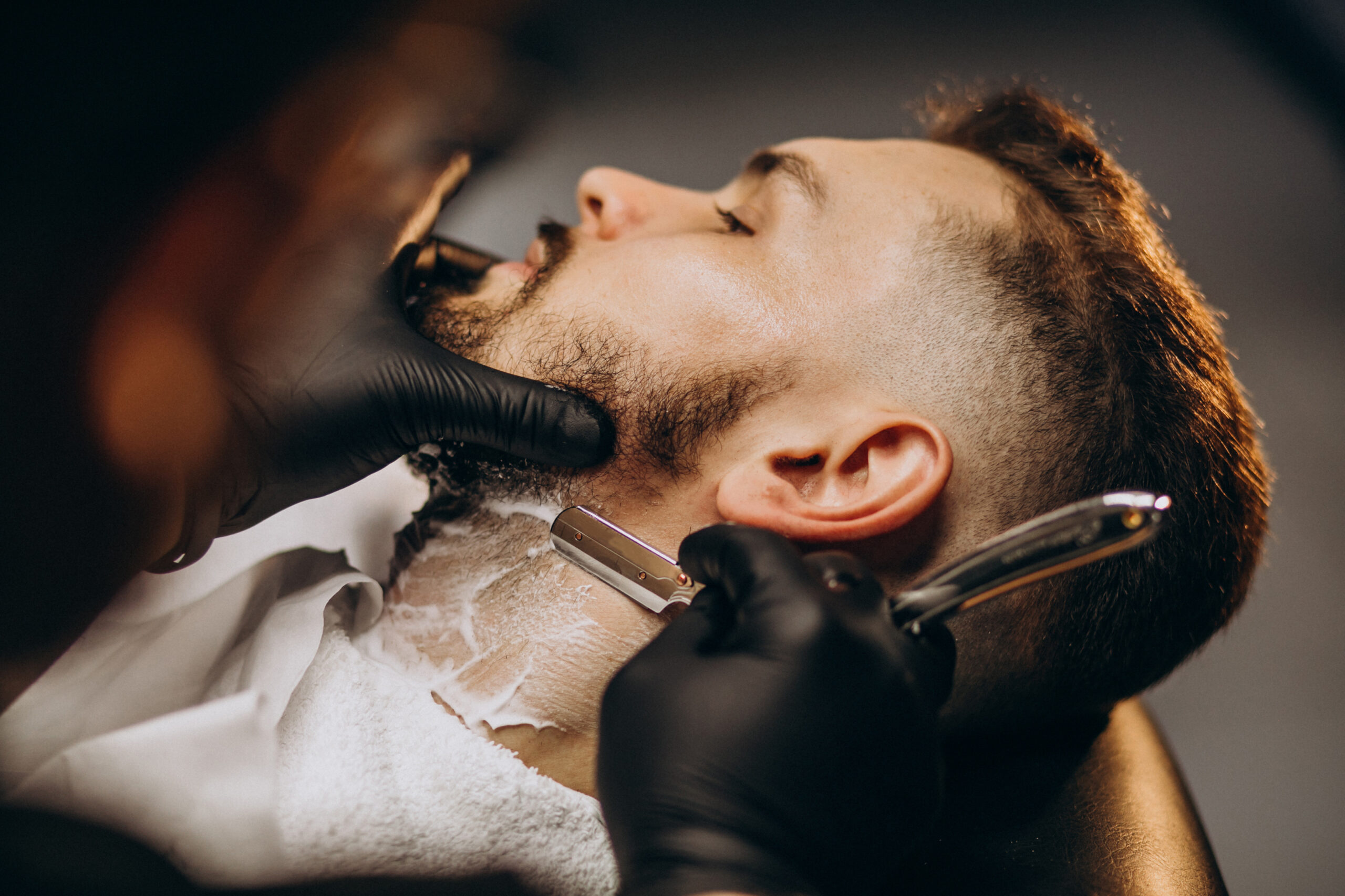 Handsome man cutting beard at a barber shop salon