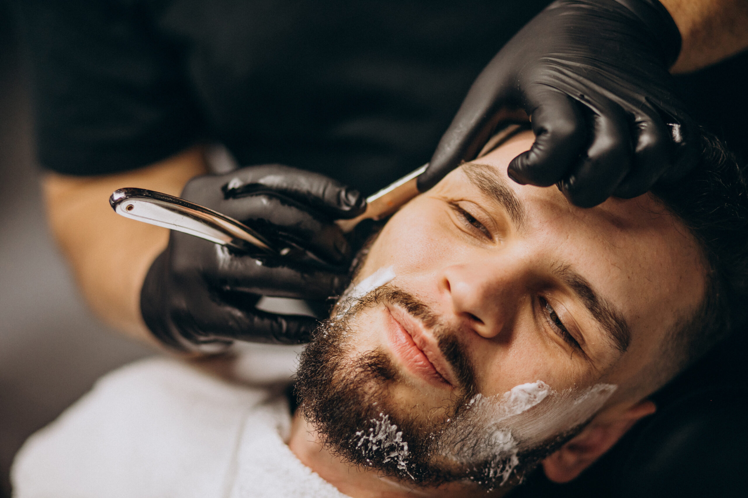 Handsome man cutting beard at a barber shop salon